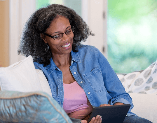 Picture: Smiling woman with glasses sitting on couch looking at tablet