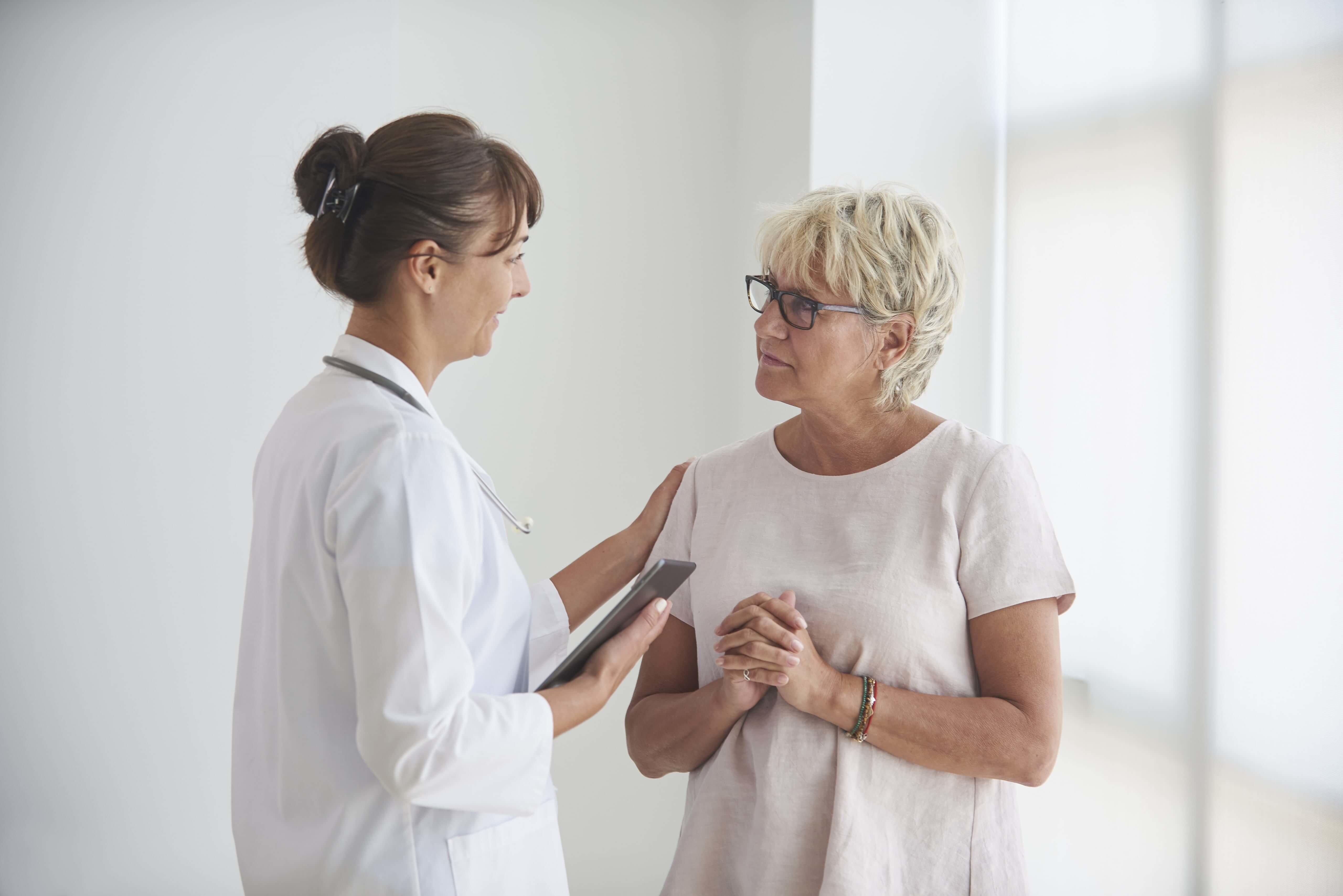 Female doctor patting the shoulder of woman wearing glasses while speaking