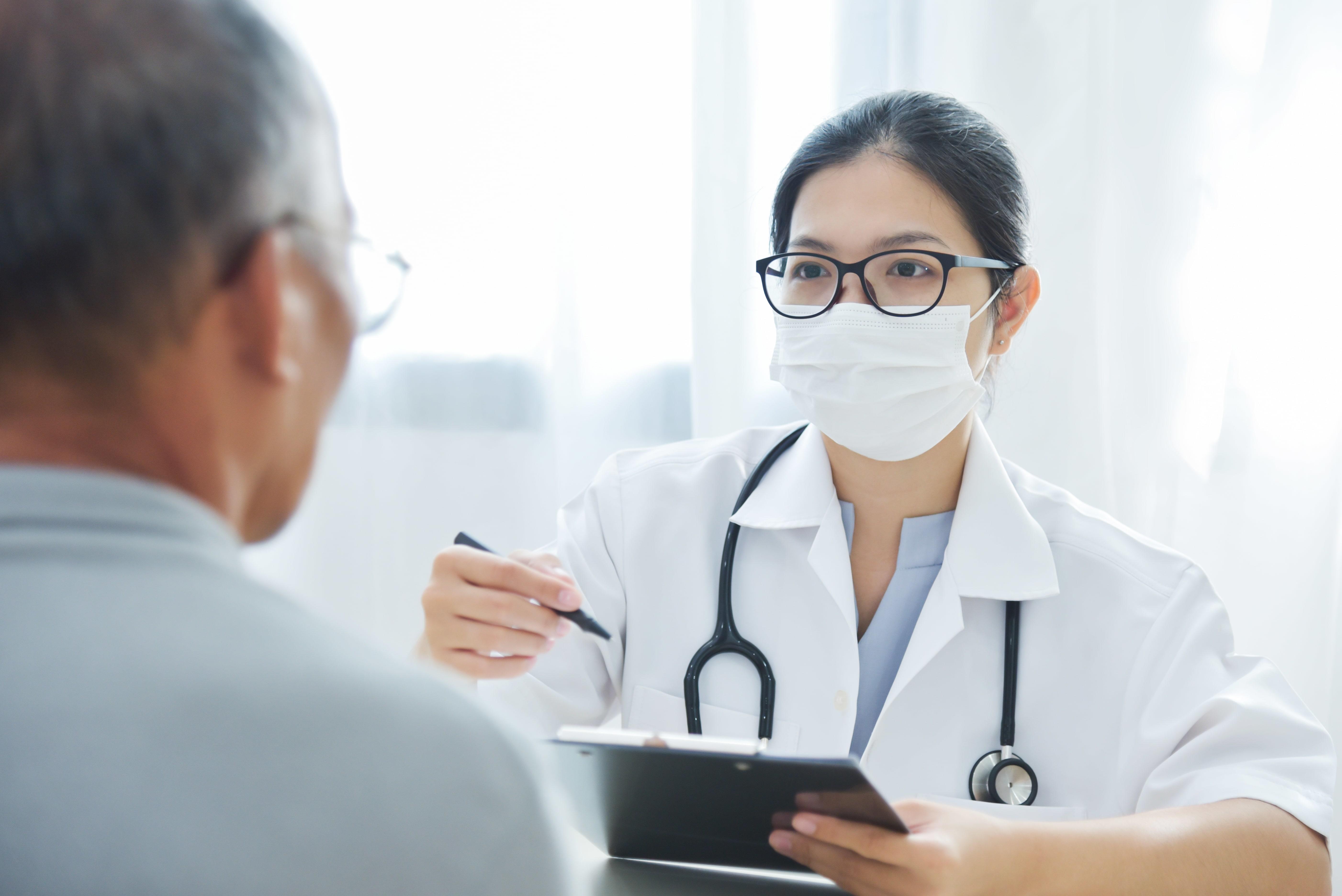 Man wearing glasses looking at doctor wearing glasses and a face mask and holding chart