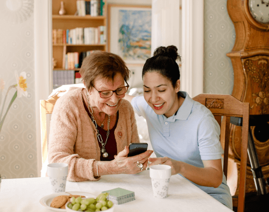 A young woman helping an older woman learn to use her smartphone at a table.