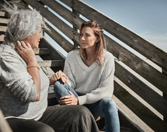 A young woman holding her mother’s hand as they sit and talk outside.